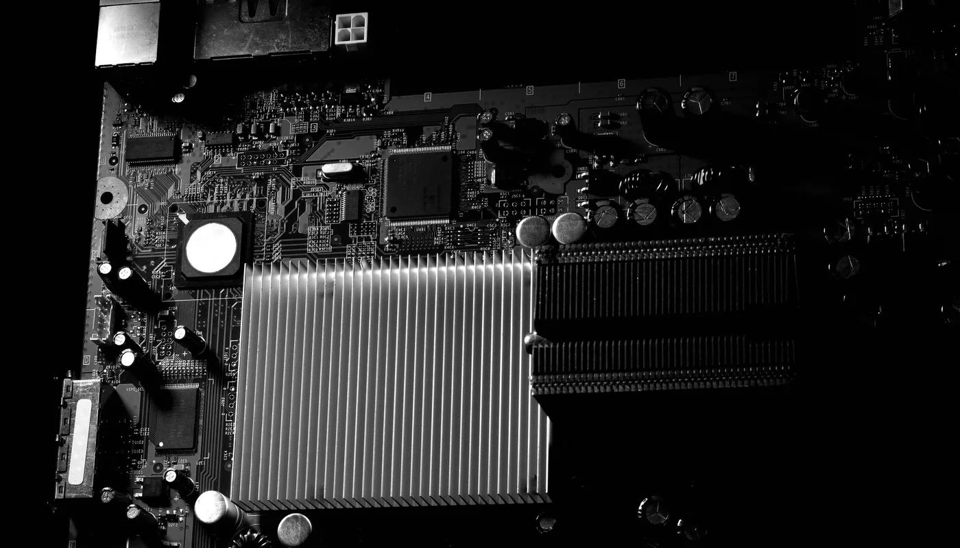 Close-up of a large aluminium fin stack mounted on a densely populated circuit board, lit from one side.