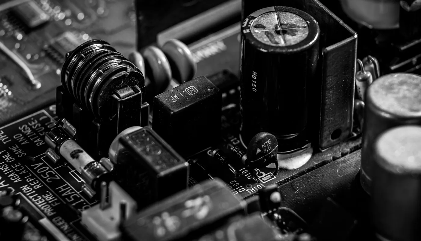 Monochrome macro of a power supply board showing electrolytic capacitors, a fuse, and an NTC thermistor among the components.
