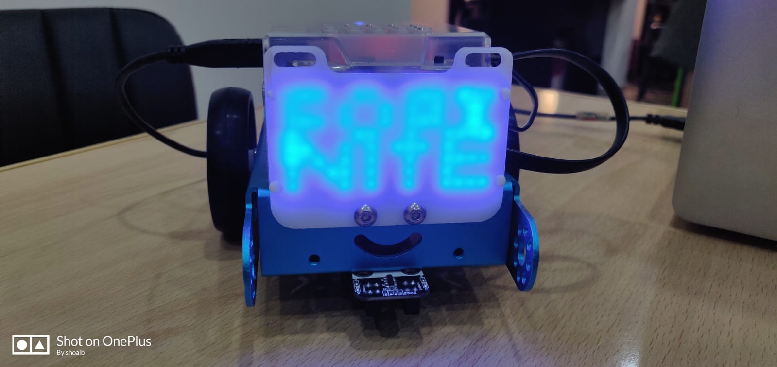A small robot with a glowing pixel face built by a child in robotics class